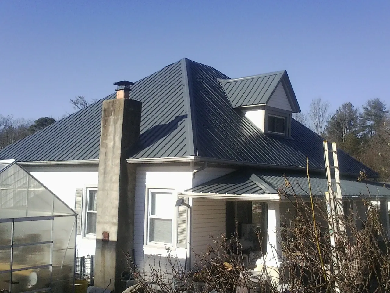 Dark blue standing seam metal roof on a white farmhouse with dormer — Slate & Tile Roof Repair by Roofing Brothers in West Rutland