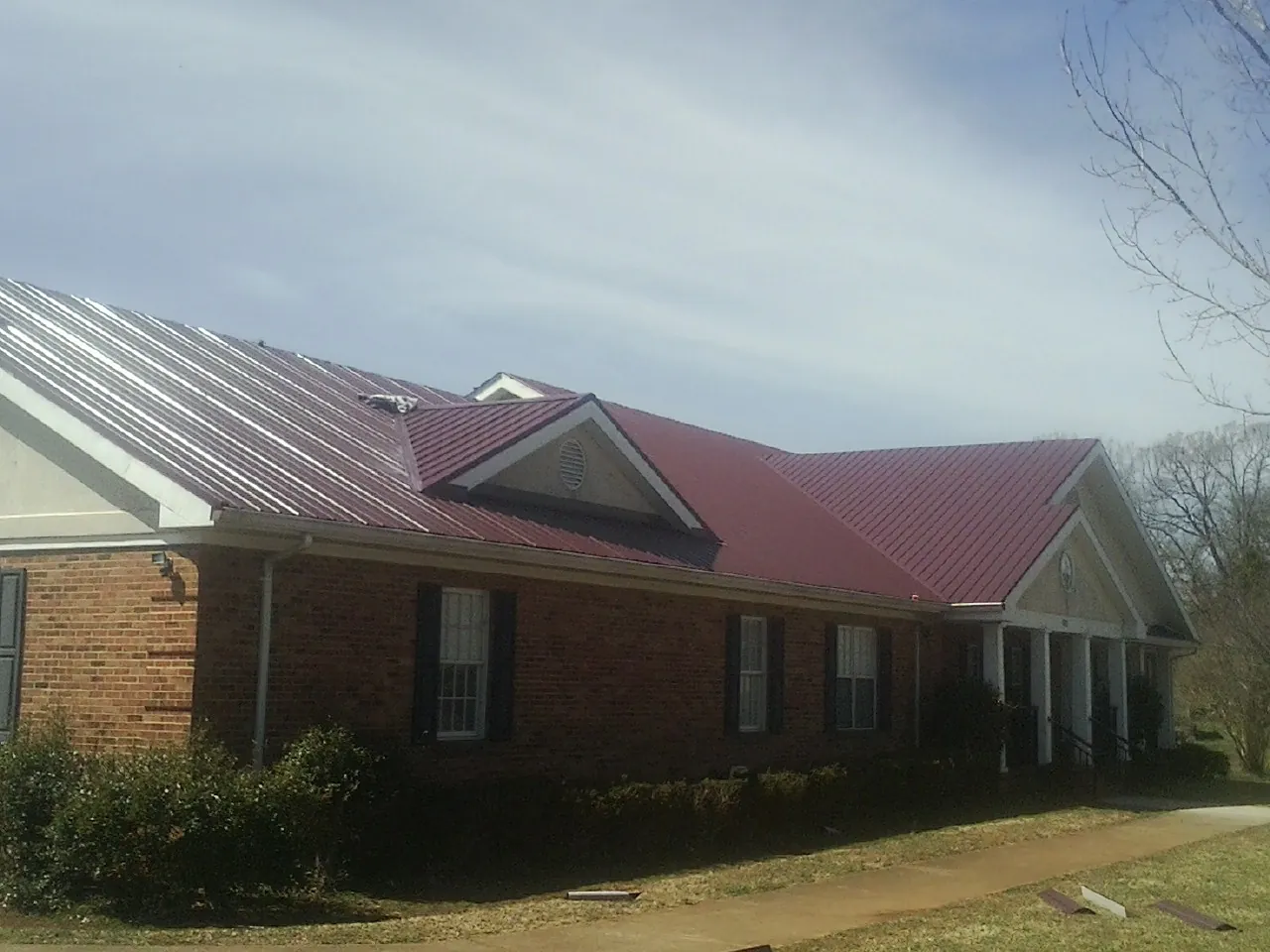 Red metal roof with gabled entries on a long brick building, from a Hail Damage Roof Repair job in West Rutland