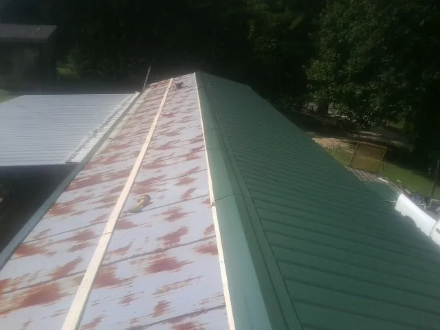Old rusted panels beside newly installed green metal roofing — Wind Damage Roof Repair by Roofing Brothers in West Rutland