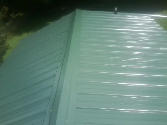 New green metal panels meeting at the ridge of a roof — Flat Roof Repair work by our crew in West Rutland