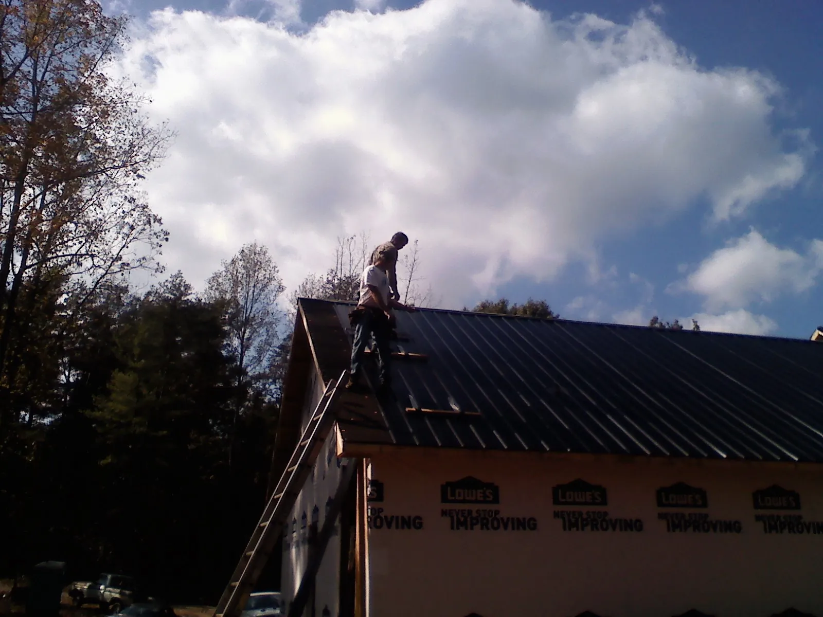 Roofer fastening dark metal panels high against a cloudy sky, from a Roof Inspection job in West Rutland