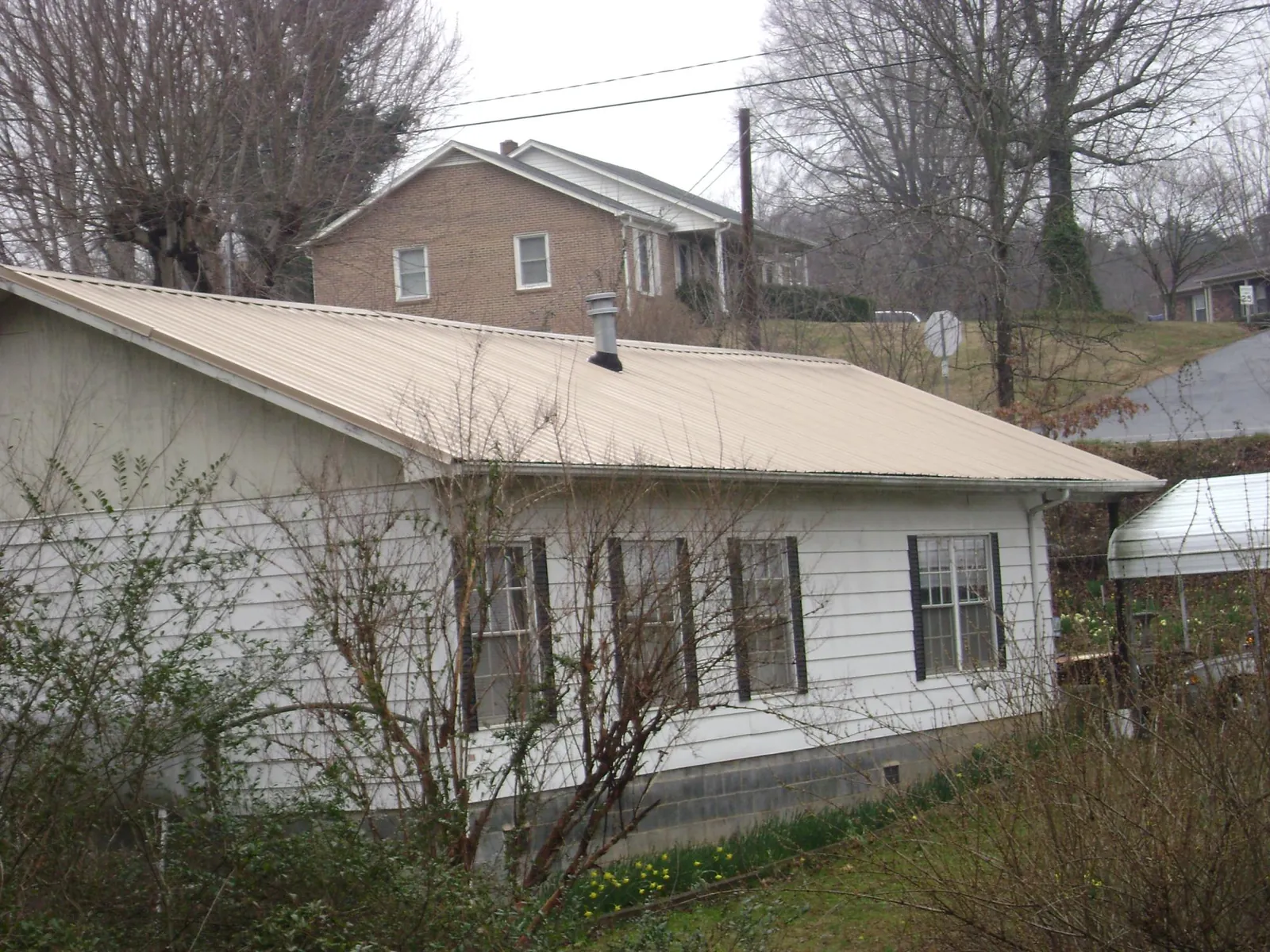 Tan metal roof on a white sided house set into a hillside — Commercial Roofing by Roofing Brothers in West Rutland